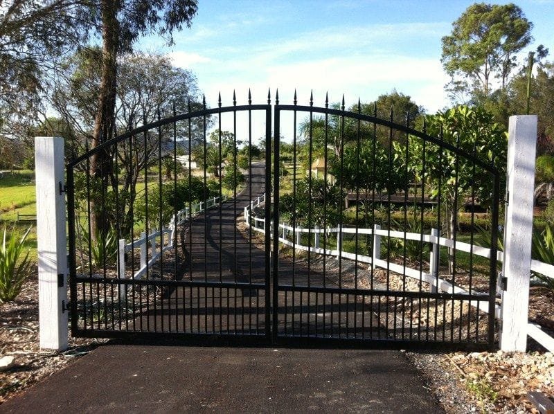 Custom wrought-iron double driveway gate opening to a tree-lined path